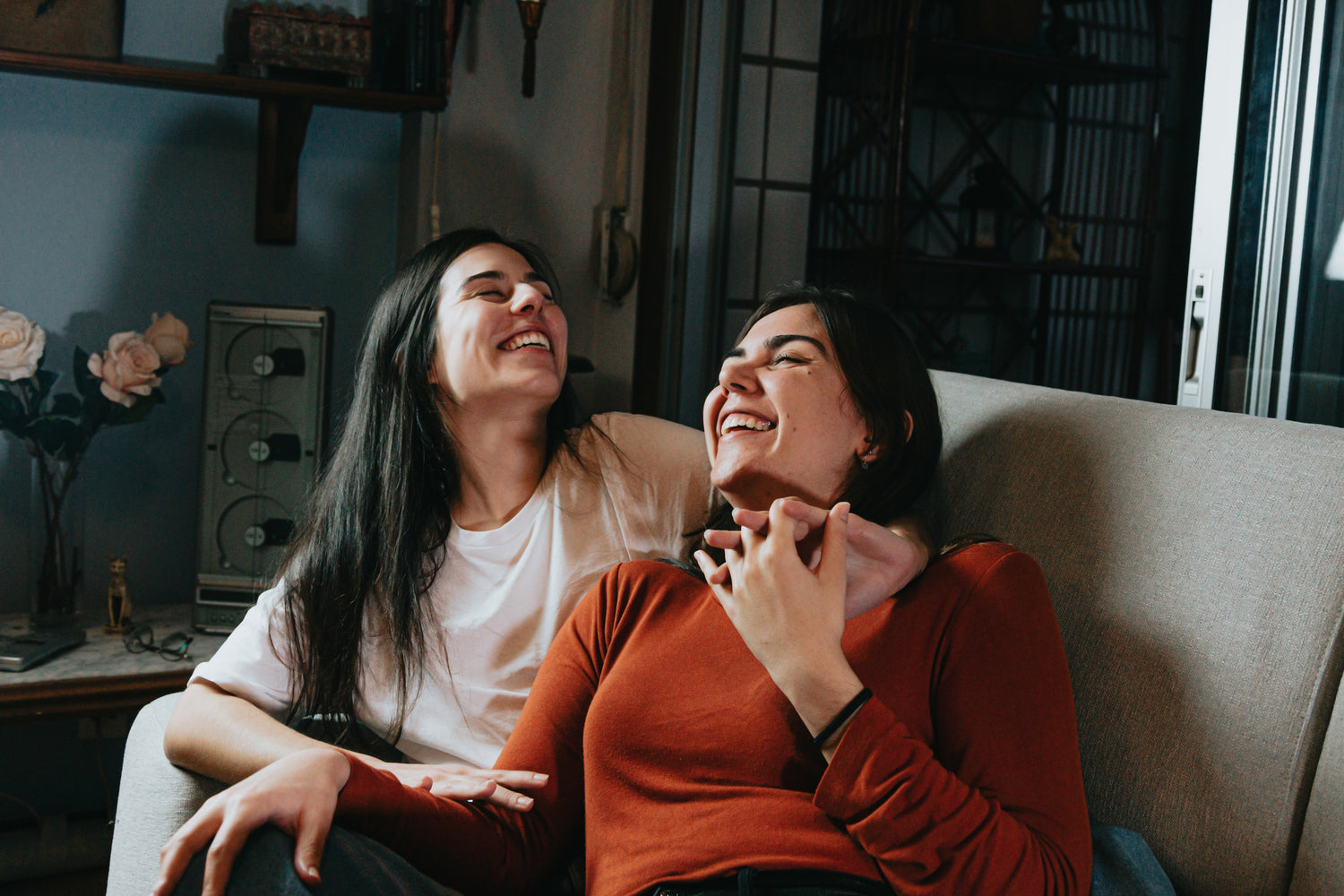 Two women sitting on a couch holding hands and laughing